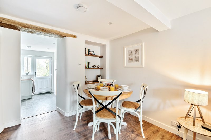 Dining area with round wooden table, white chairs, and tripod floor lamp