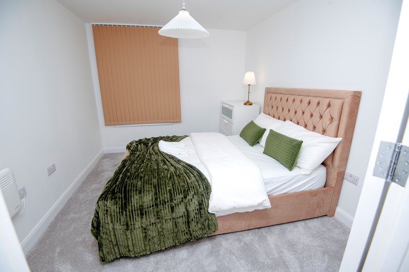 Modern bedroom with upholstered bed, white bedding, green cushions and throw blanket