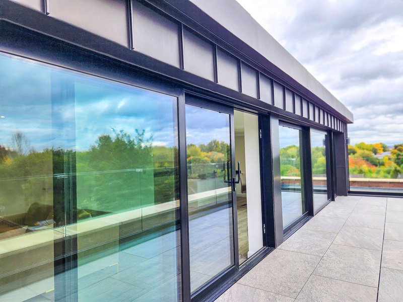 Modern building exterior with floor-to-ceiling glass doors and windows overlooking garden landscape
