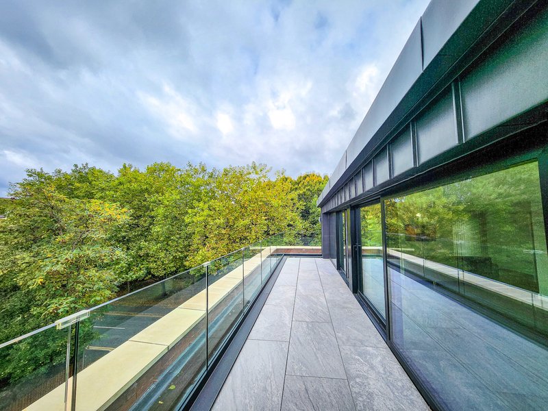 Modern balcony with glass railing overlooking green trees and sky