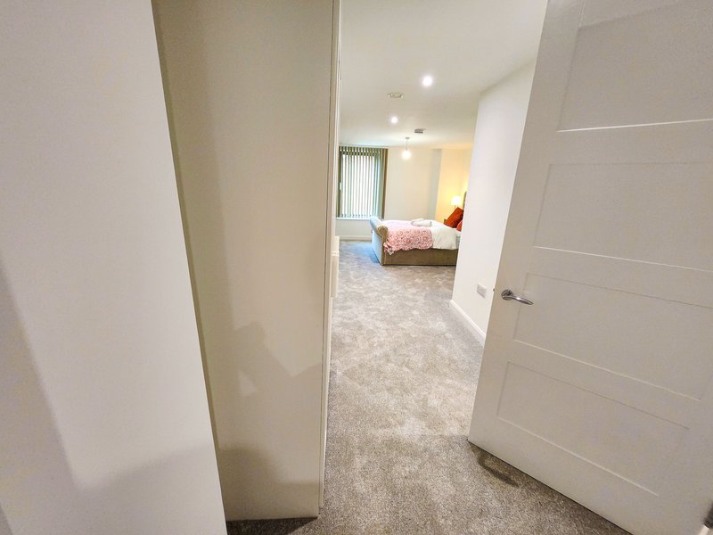 Hallway with white doors and walls, carpeted flooring, leading to bedroom with bed visible