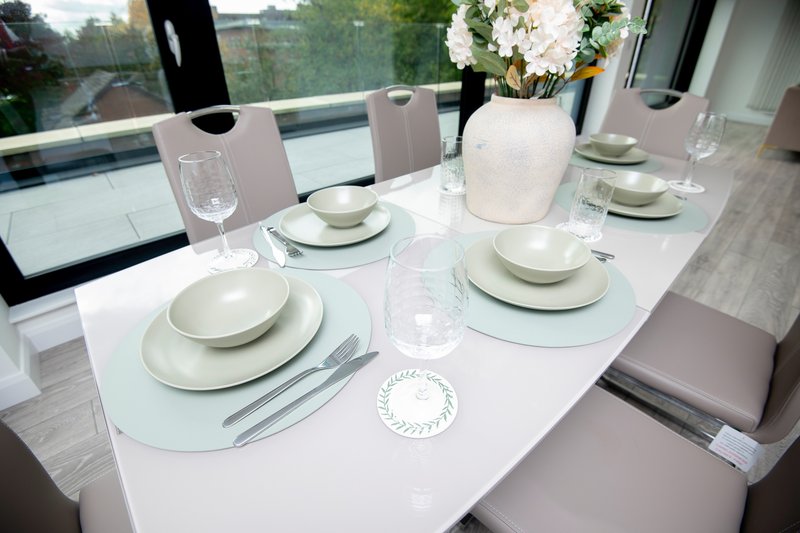 Modern dining table set for six with white plates, glasses and white flower arrangement
