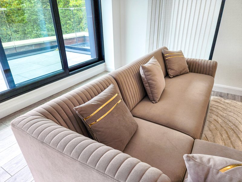 Modern living room with beige upholstered sofa, cushions, and large windows overlooking pool area