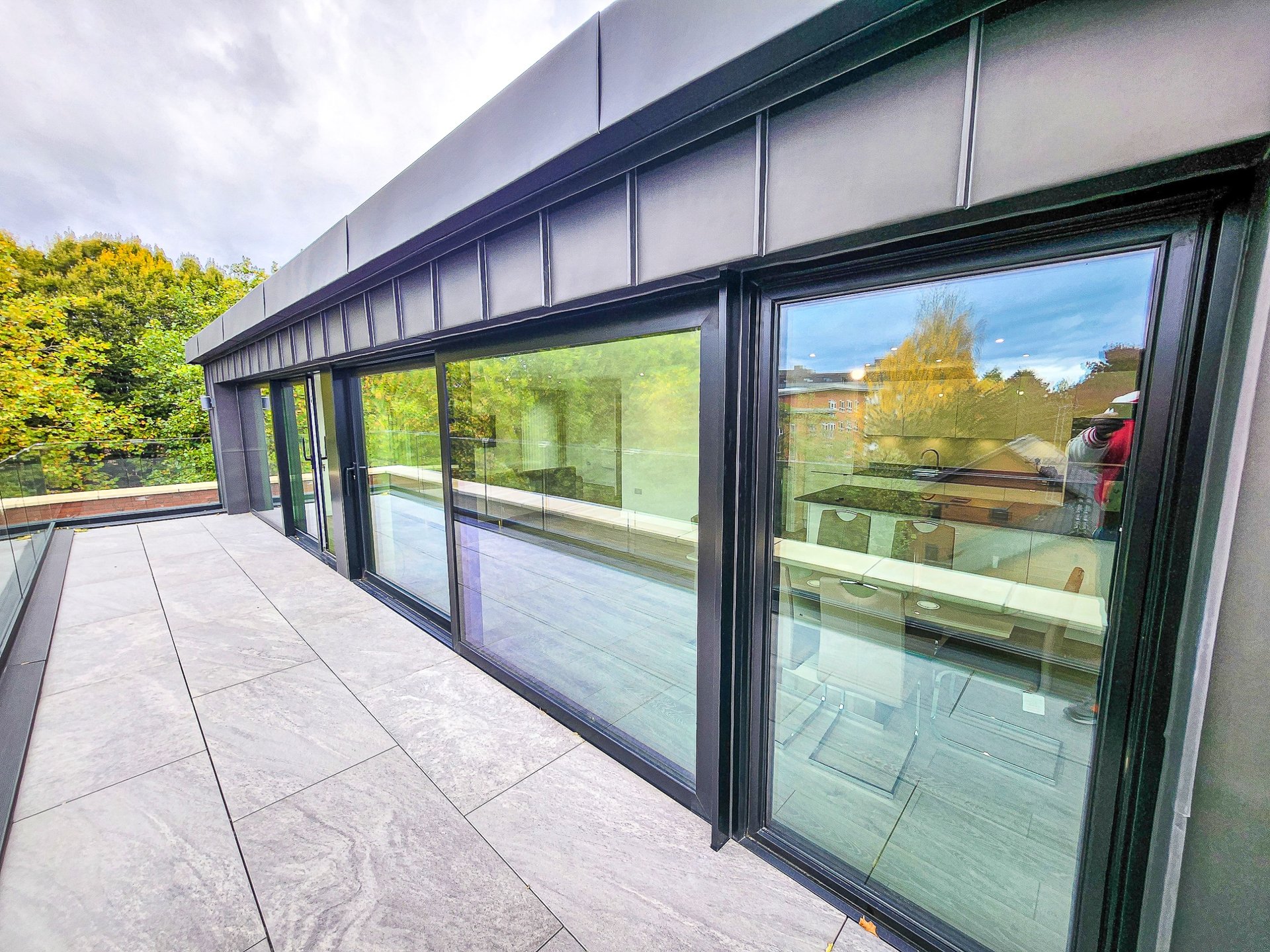 Modern building exterior with large glass sliding doors and paved terrace overlooking green landscape