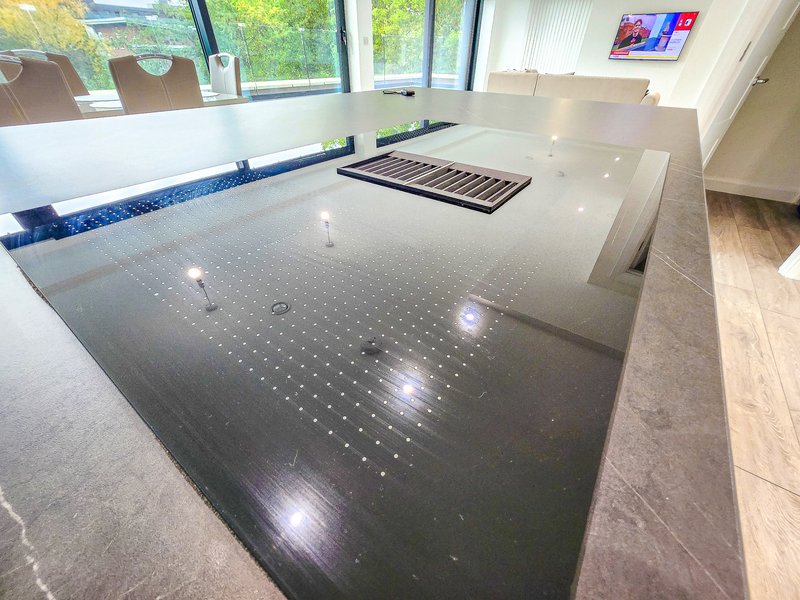 Modern kitchen with large dark countertop, keyboard, windows, and light wood flooring