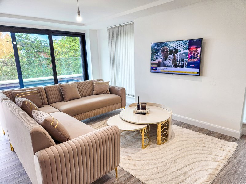 Modern living room with two beige sofas, round coffee table, wall-mounted TV, and garden views