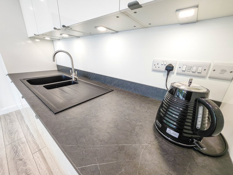 Modern kitchen with dark countertop, sink, faucet, kettle and white cabinetry