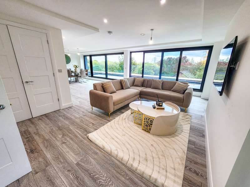 Modern living room with corner sofa, round coffee table, large windows and wooden flooring