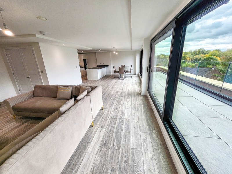 Modern open-plan living space with brown sofa, wooden flooring, large windows overlooking garden