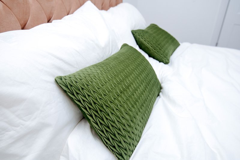 Bedroom bed with white linens, green decorative pillows and pink headboard