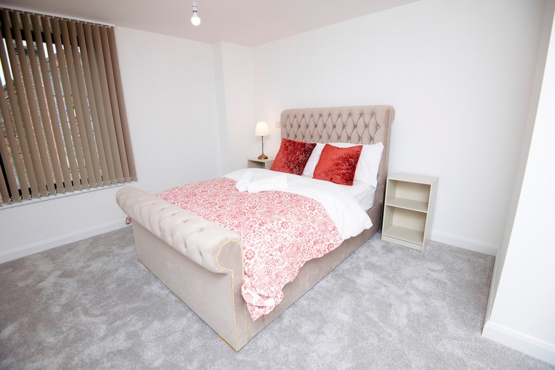Bright bedroom with upholstered bed, pink bedding, red cushions, and neutral carpet