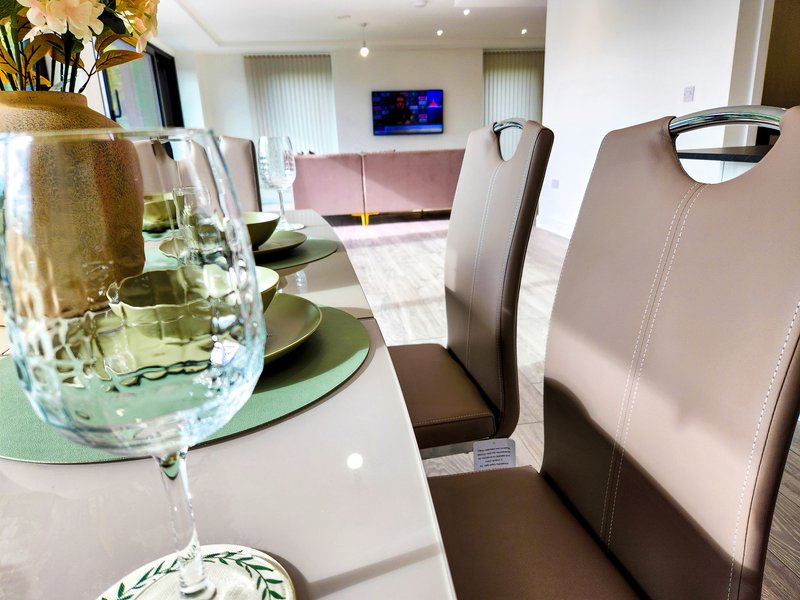 Modern dining area with white table, upholstered chairs, and open-plan living room view