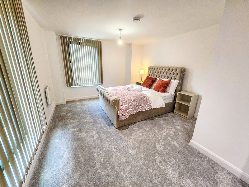 Spacious bedroom with double bed, upholstered headboard, carpeted floor and vertical blinds