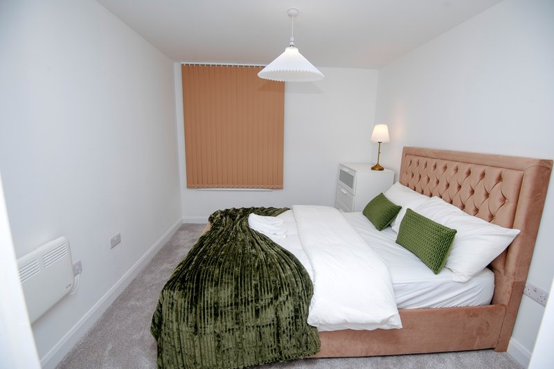 Modern bedroom with double bed, green cushions, pendant light and bedside lamp