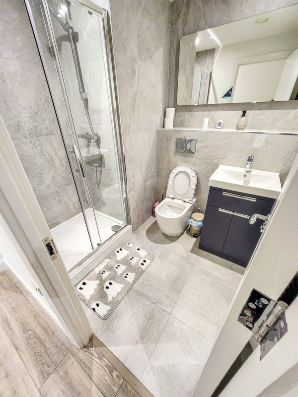 Modern bathroom with shower enclosure, toilet, vanity sink, mirror and grey tile flooring