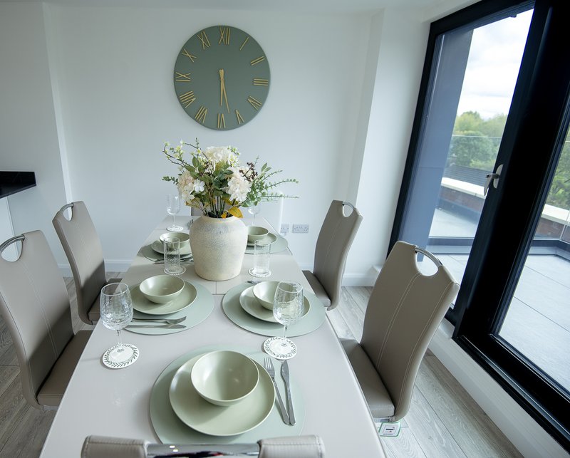 Modern dining room with white table, beige chairs, place settings, wall clock and large windows