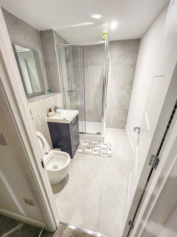 Modern bathroom with walk-in shower, white toilet, dark vanity sink, and tile flooring