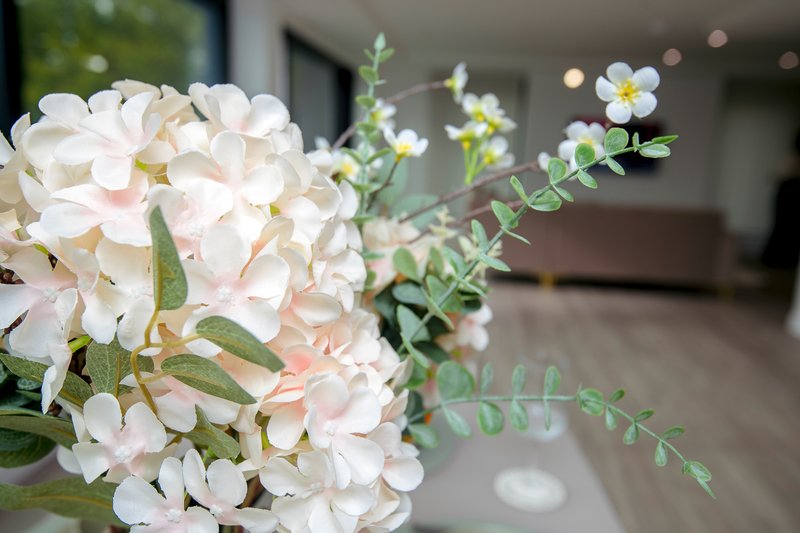 Close-up of white and pink flowers in vase with blurred interior hallway behind
