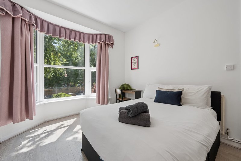 Bright bedroom with double bed, pink curtains, large window with garden view
