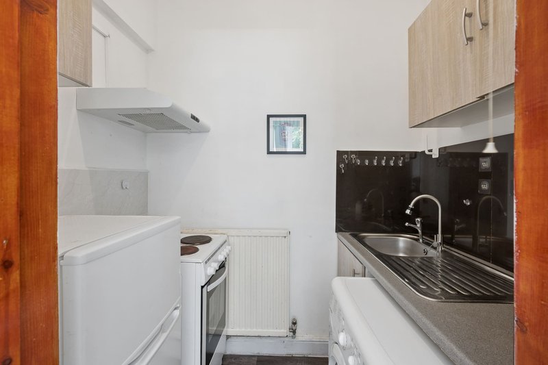 Compact galley kitchen with white appliances, black backsplash, and wooden cabinetry