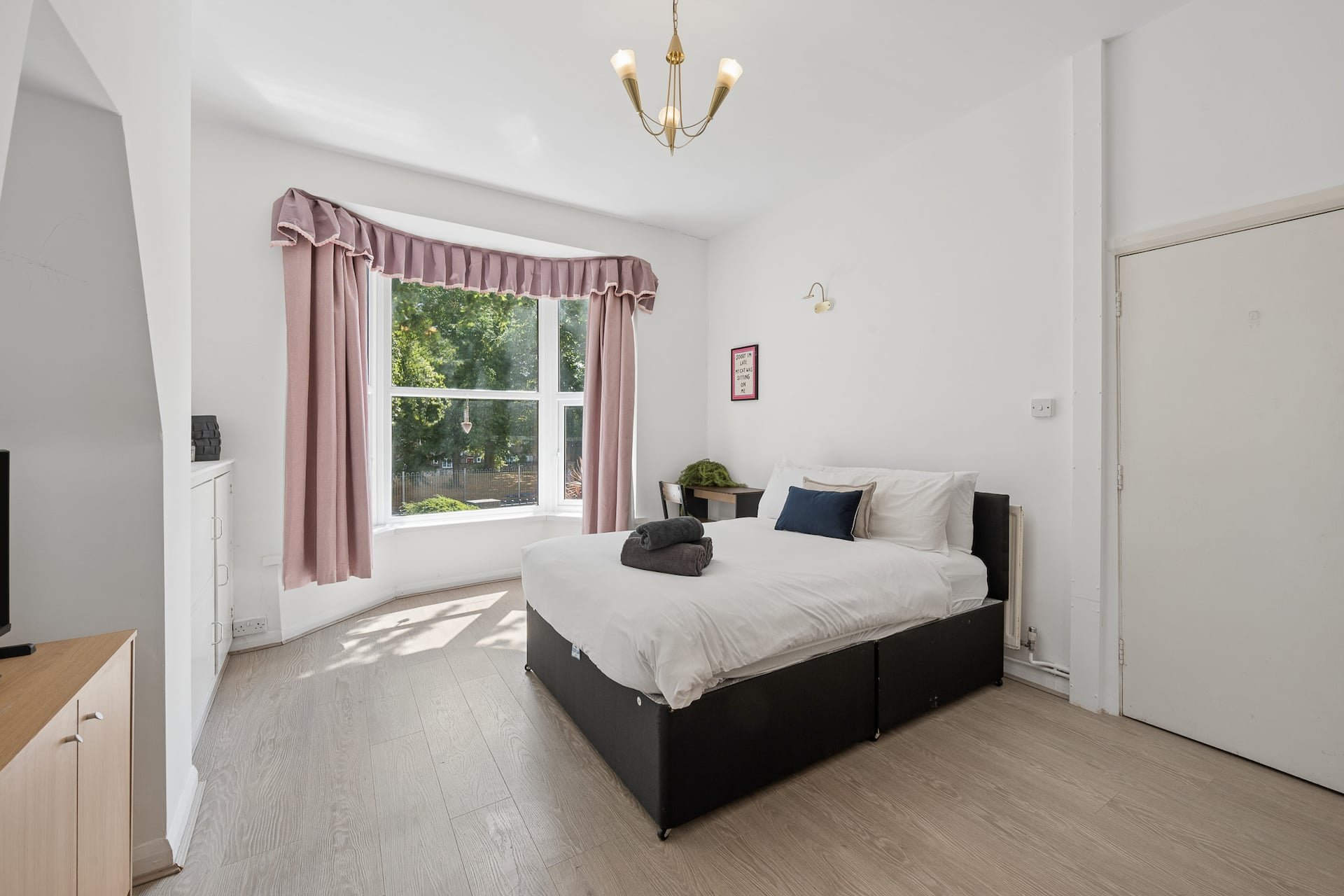 Bright bedroom with double bed, pink curtains, wooden floor and pendant light
