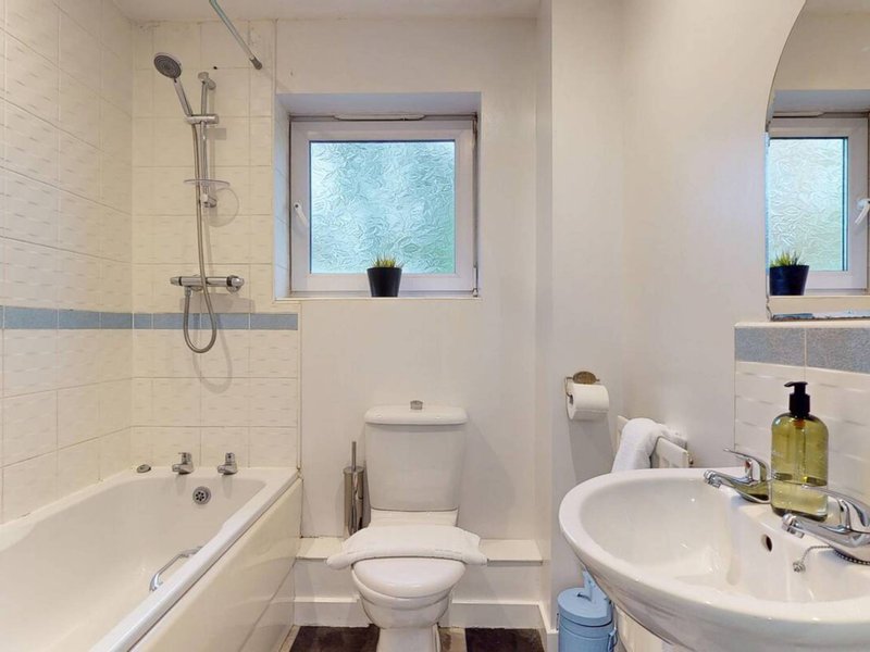 Clean bathroom with bathtub, toilet, pedestal sink and windows overlooking garden