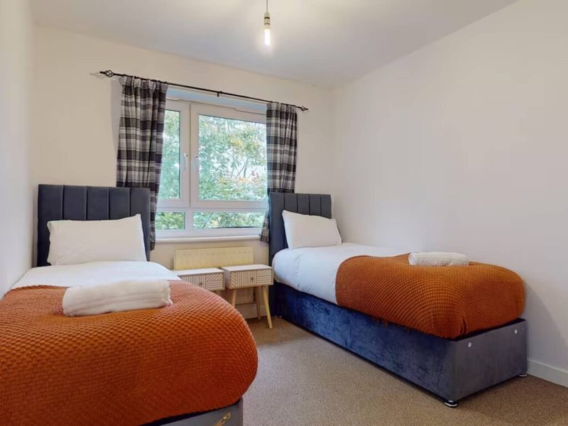 Twin bedroom with two single beds, orange throws, checkered curtains and window view