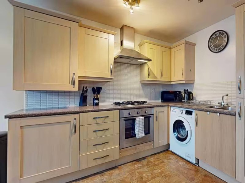 Modern kitchen with cream cabinets, built-in oven, gas hob, white washing machine, and tiled backsplash