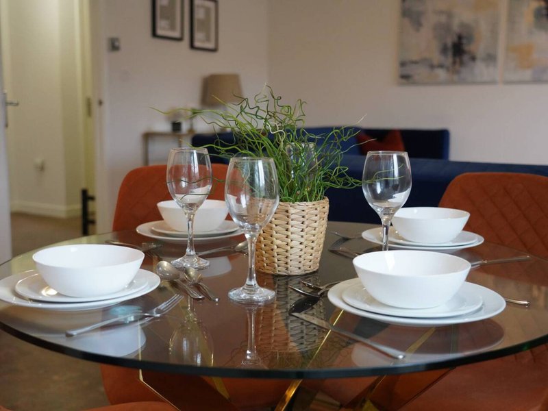Dining table set for four with white plates, glasses, and potted plant centerpiece