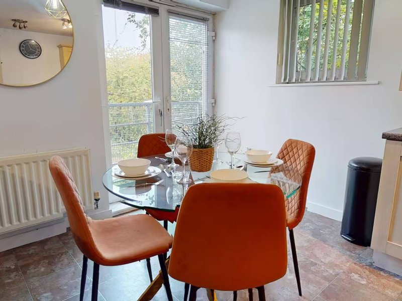 Bright dining room with glass table, orange upholstered chairs, and garden views through patio doors
