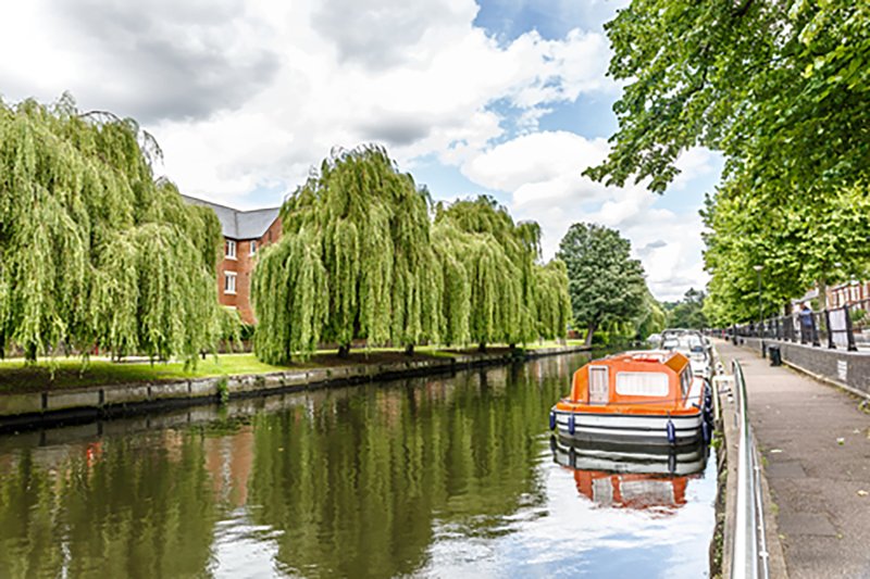 Canal-side property with moored orange boat, weeping willow trees and brick building