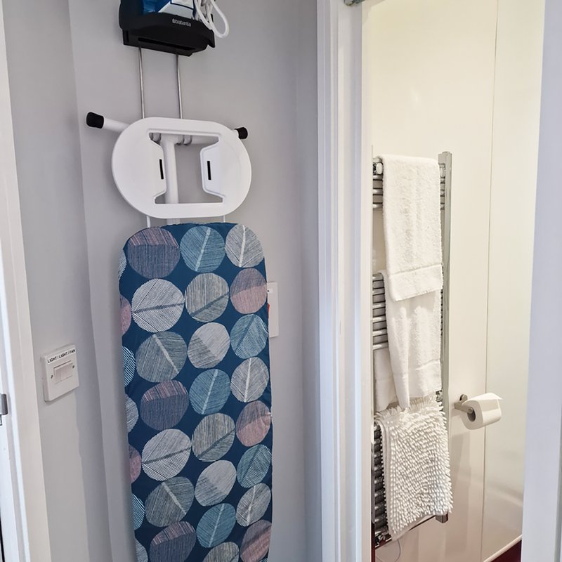 Bathroom wall with ironing board, towel rail with folded towels, and storage basket