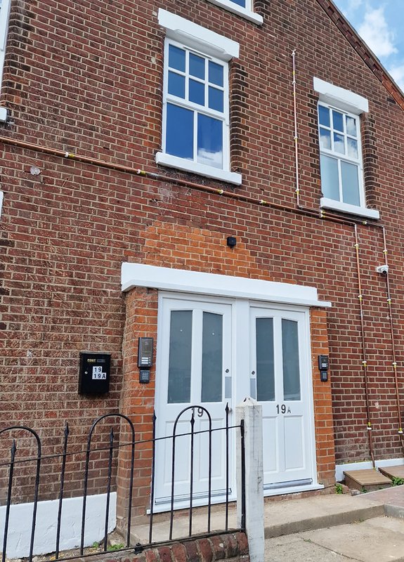 Red brick terraced house with white-framed windows, white door, and metal railings