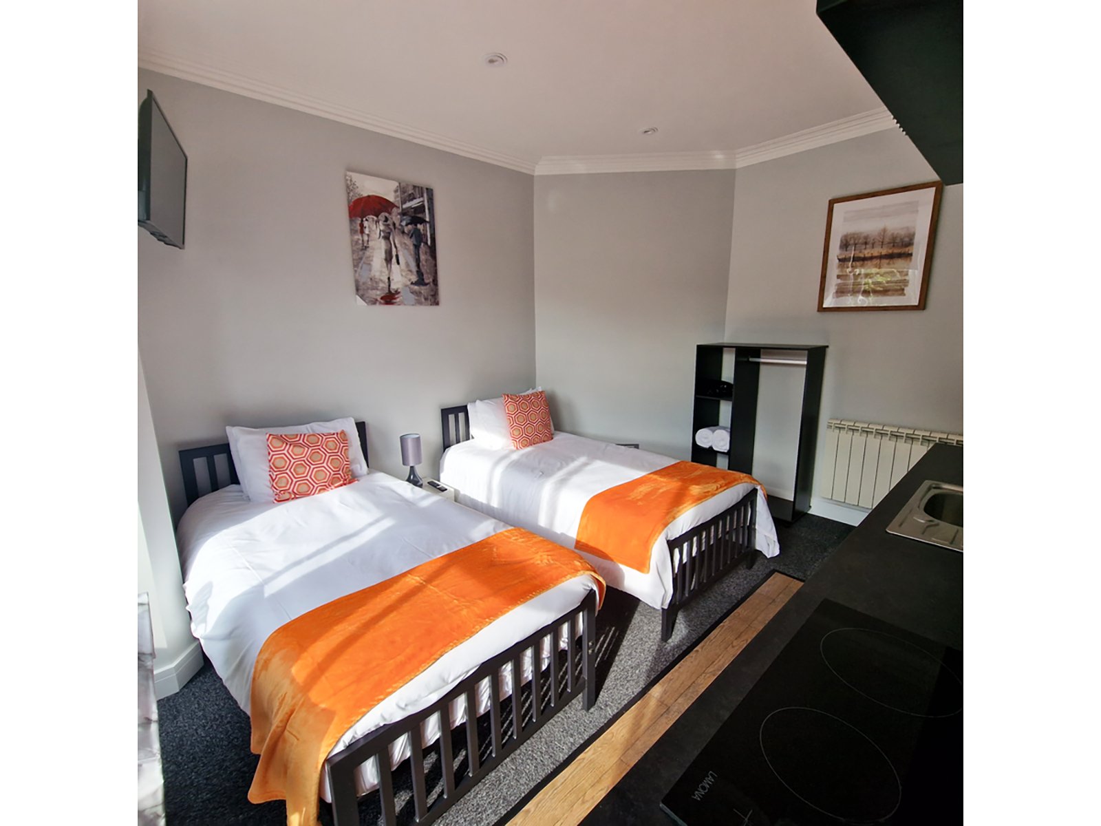 Twin bedroom with two single beds, orange blankets, white bedding, and framed wall art