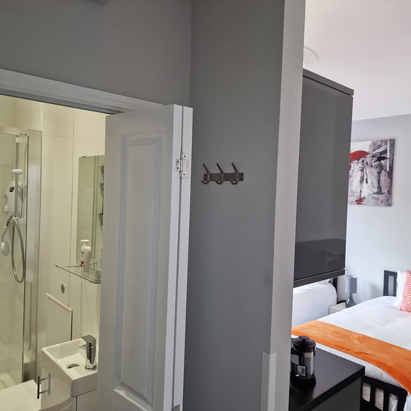 Modern bedroom with ensuite shower room, double bed with orange throw, grey and white walls