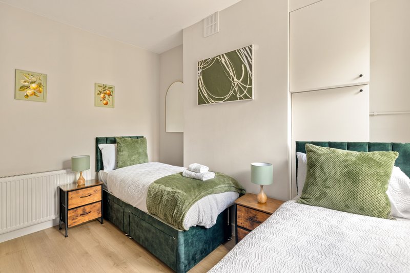 Bright twin bedroom with green bedding, wooden nightstands, wall art and radiator