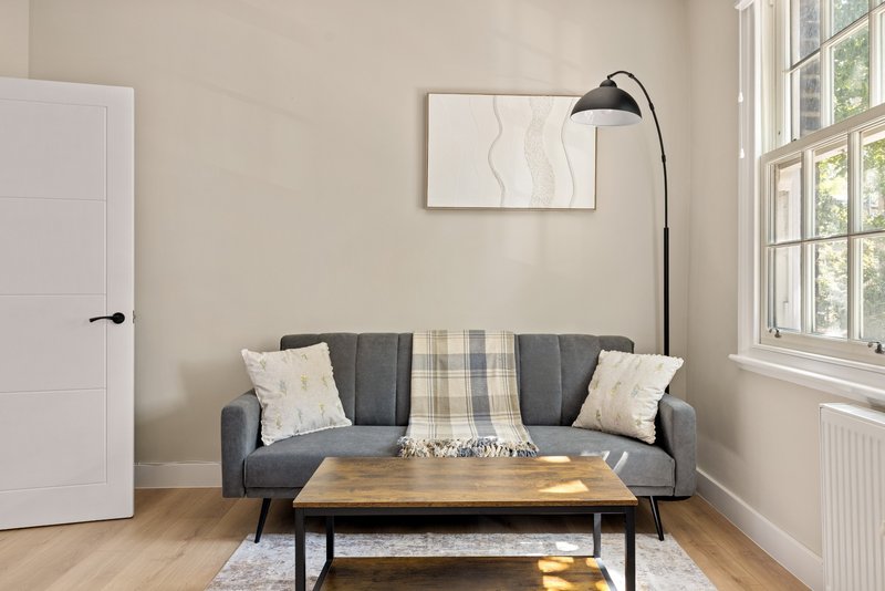 Light living room with grey sofa, wooden table, arc lamp and framed wall art