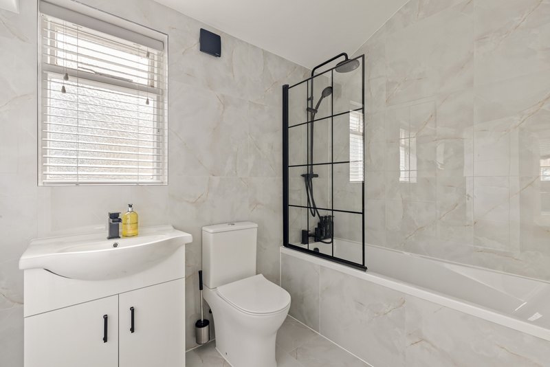 Modern bathroom with white vanity, toilet, bathtub, and black-framed shower screen