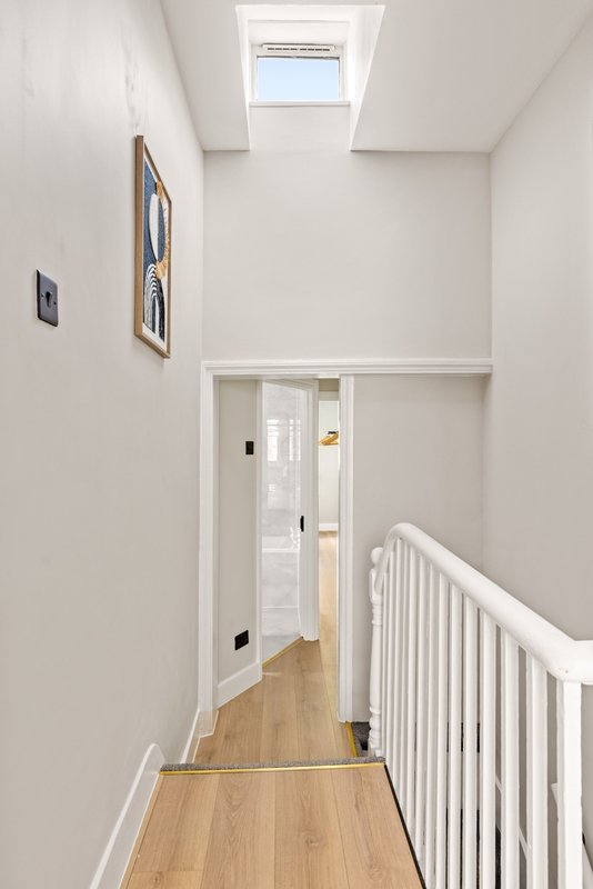 Bright hallway with skylight, white walls, wooden flooring and white stair railing