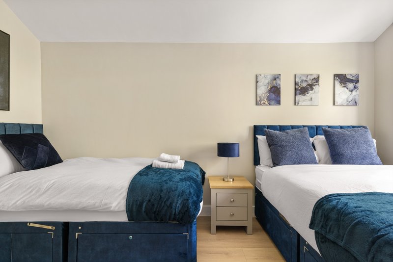 Twin bedroom with two beds, blue bedding, wooden nightstand and framed wall art