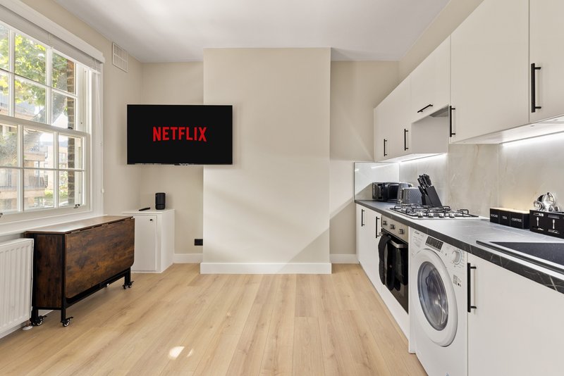 Modern kitchen with white cabinetry, wood flooring, washing machine, and wall-mounted TV