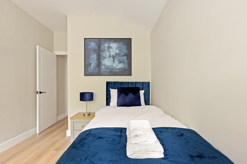 Modern bedroom with double bed, blue headboard, white pillows, wooden floor and framed wall art
