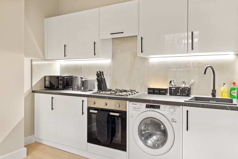 Modern white kitchen with built-in oven, washing machine, and black countertop