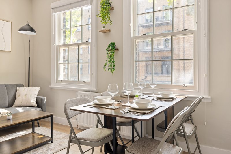 Bright dining room with set table, chairs, sofa, and large windows overlooking street