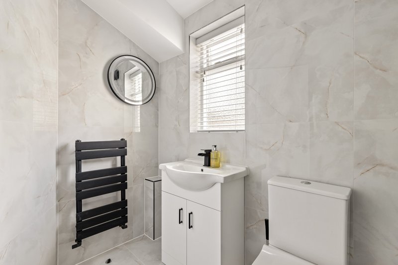 Modern bathroom with white vanity, black heated towel rail, round mirror and window