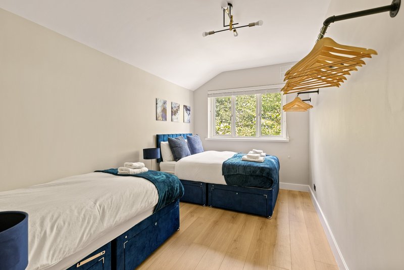 Twin bedroom with navy storage beds, wooden floor, window with garden view and pendant lighting