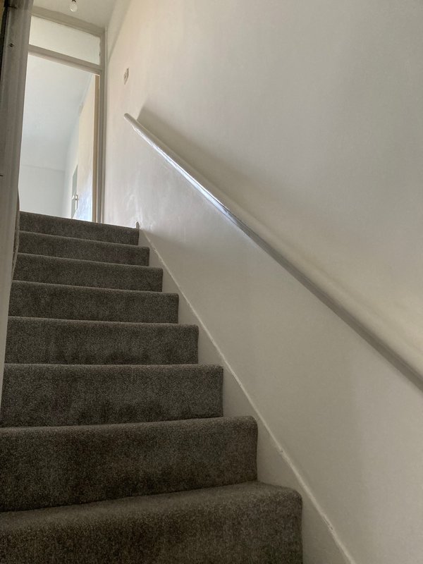 Carpeted staircase with gray treads and white painted walls with handrail