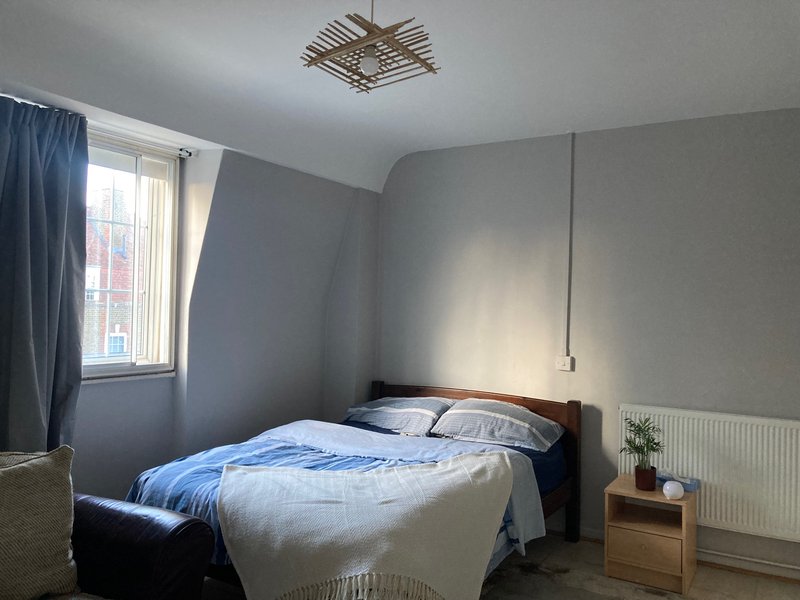Bedroom with double bed, blue bedding, wooden headboard, window with curtains, radiator