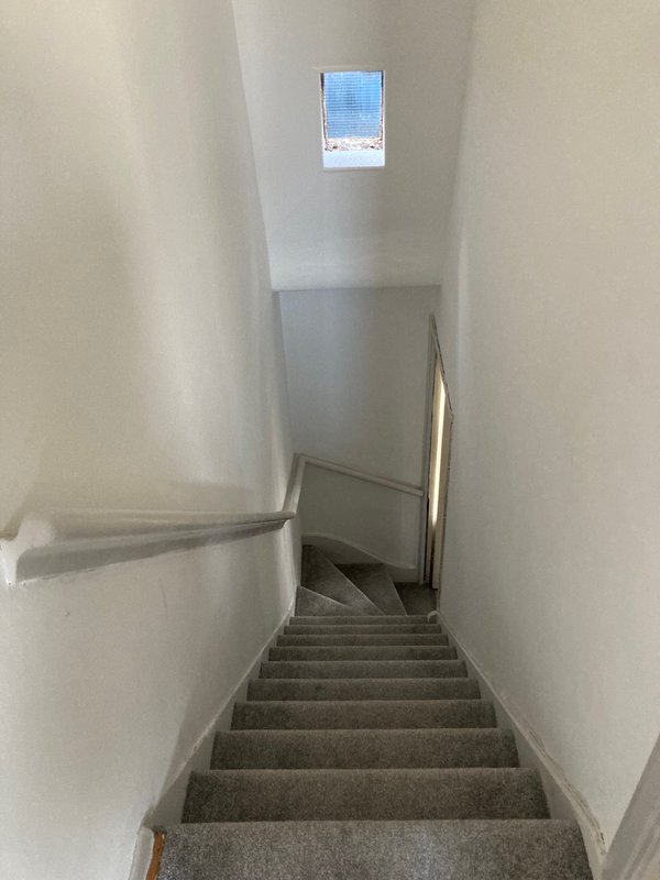 Staircase with gray carpet, white walls, metal handrail, small window above