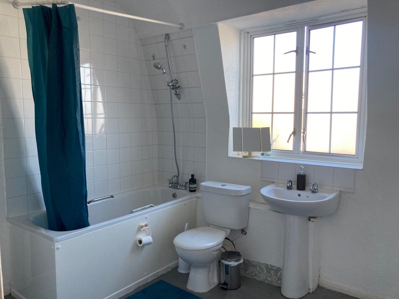 Bright bathroom with bathtub, shower curtain, toilet, pedestal sink and window